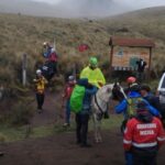 Um grupo de pessoas em uma trilha montanhosa com resgatadores e um cavalo próximo a uma ambulância