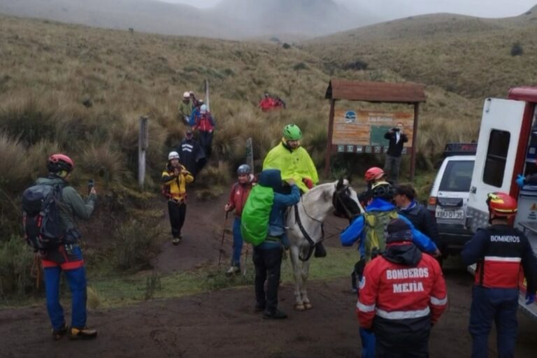Um grupo de pessoas em uma trilha montanhosa com resgatadores e um cavalo próximo a uma ambulância