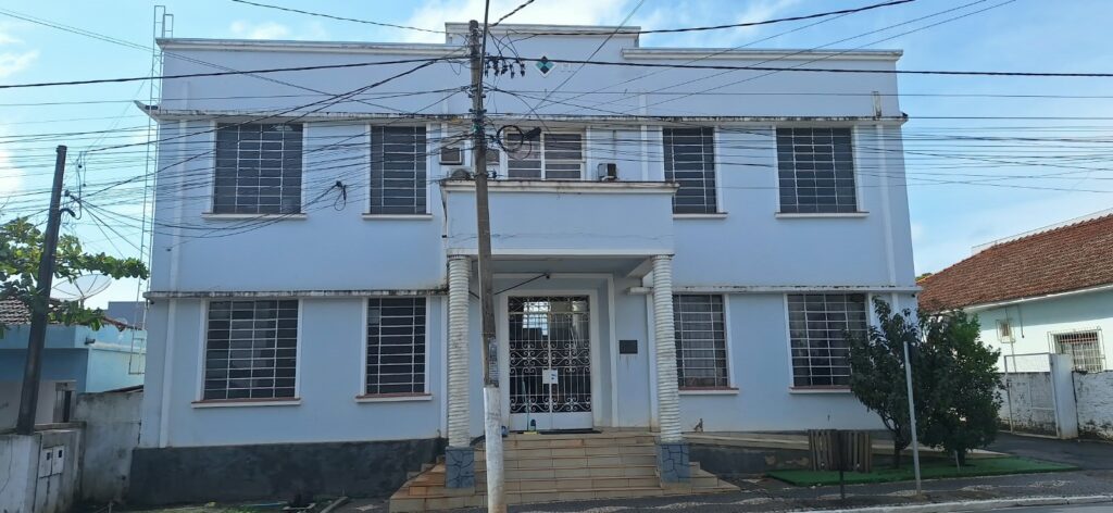 Um prédio branco com colunas e grades na entrada sob fios elétricos em dia claro