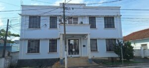 Um prédio branco com colunas e grades na entrada sob fios elétricos em dia claro