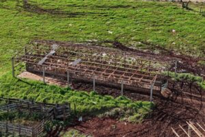 Um galpão em construção em meio a um campo verde com solo exposto