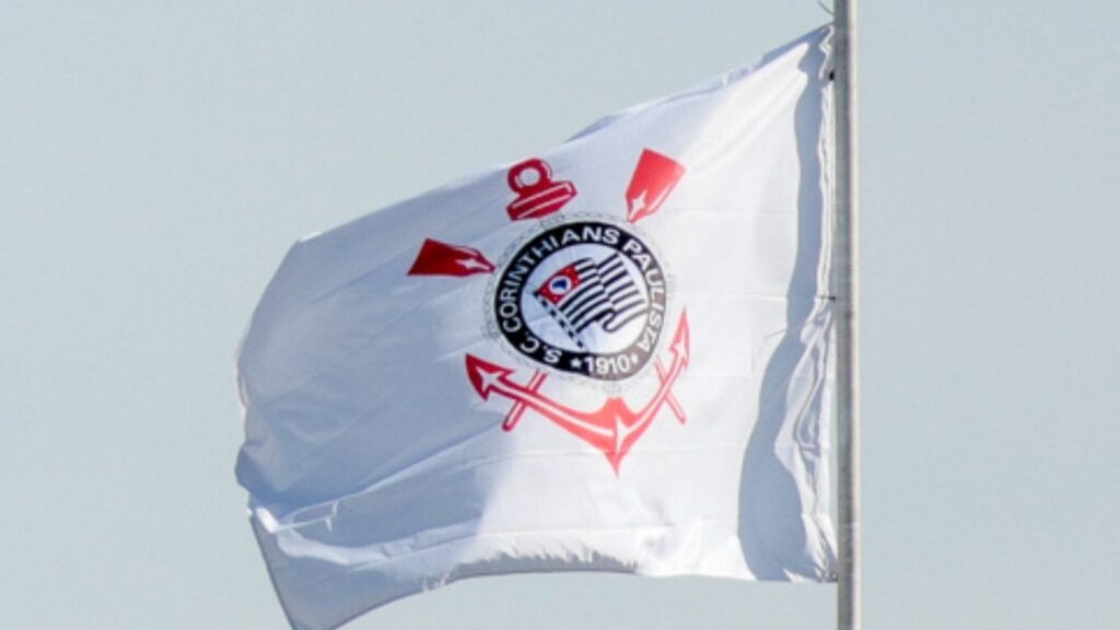 Bandeira do Corinthians com o escudo do clube tremula ao vento contra o céu claro