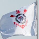 Bandeira do Corinthians com o escudo do clube tremula ao vento contra o céu claro