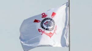 Bandeira do Corinthians com o escudo do clube tremula ao vento contra o céu claro