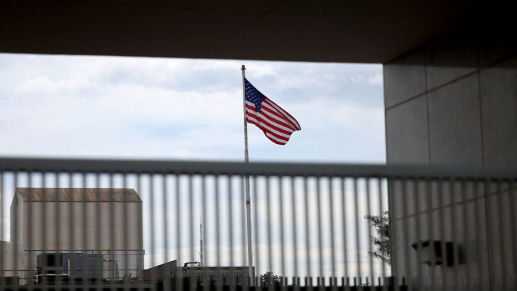 Bandeira dos Estados Unidos acena atrás de grade em edifício com estrutura metálica e concreto