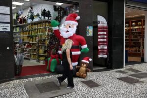 Uma mulher caminha em frente a uma loja com decoração de Natal e um boneco inflável de Papai Noel