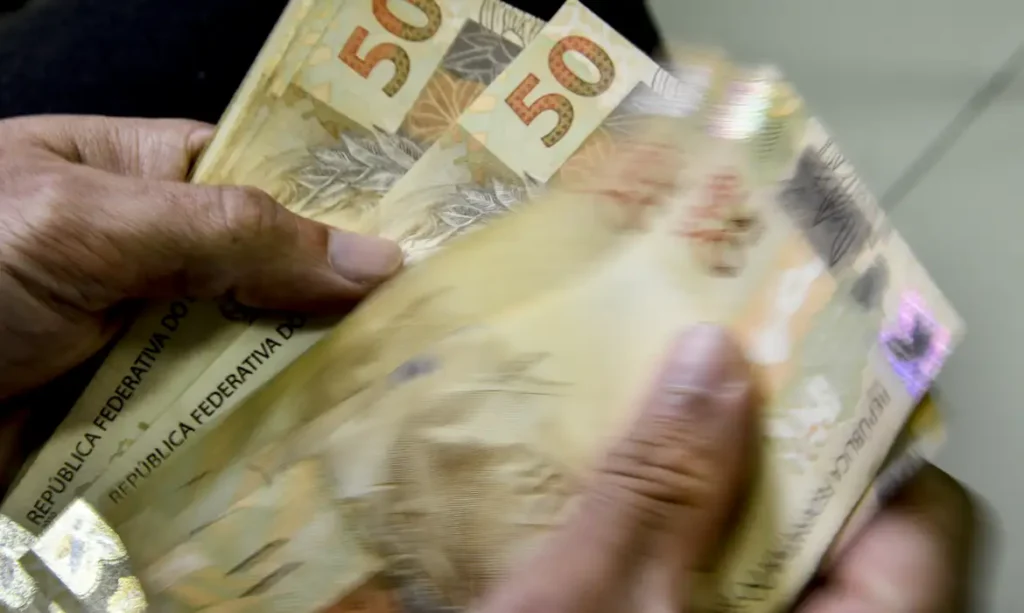 Uma pessoa conta notas de cinquenta reais com as mãos
