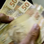 Uma pessoa conta notas de cinquenta reais com as mãos