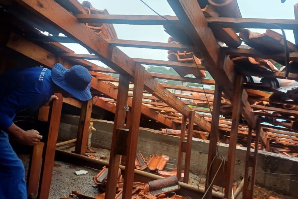 Um homem de camisa azul e chapéu trabalha em estrutura de madeira de telhado em construção