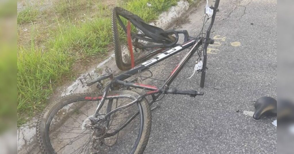 Uma bicicleta destruída e tombada na beira da estrada com o guidão quebrado e o pneu furado