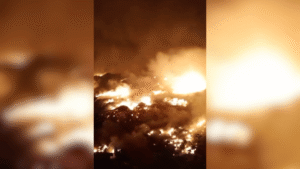 Um incêndio intenso ilumina a noite com fumaça densa e chamas altas em uma área aberta