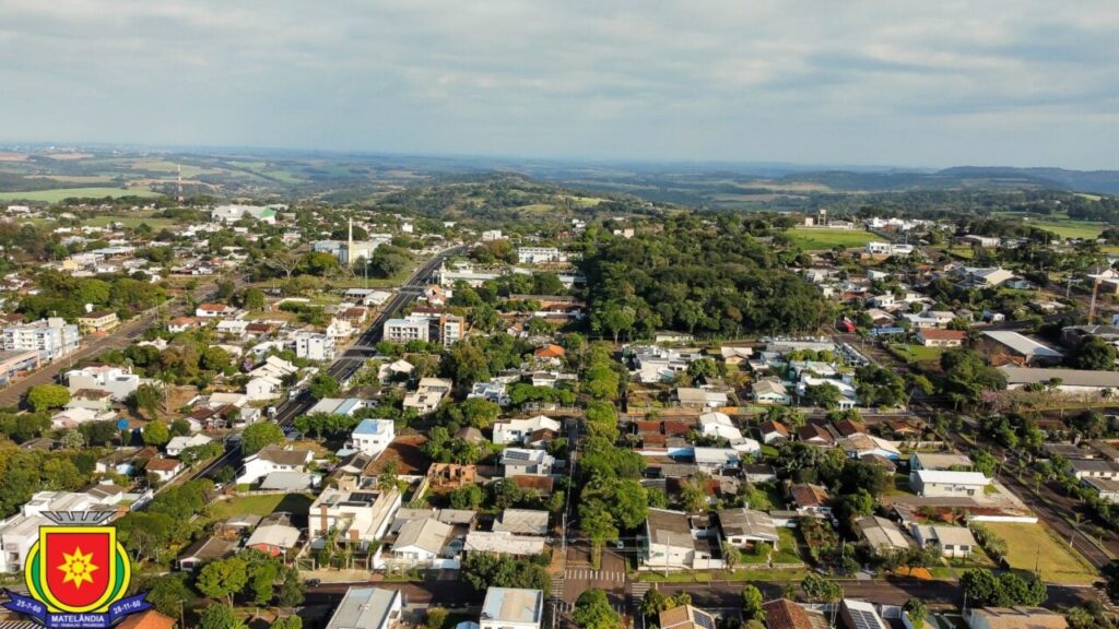 Vista aérea de uma cidade com casas, ruas e áreas verdes sob céu nublado