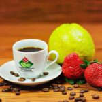 Uma xícara de café com grãos espalhados, uma fruta verde e morangos em uma superfície de madeira