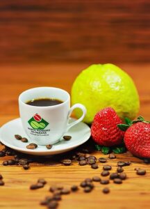 Uma xícara de café com grãos espalhados, uma fruta verde e morangos em uma superfície de madeira