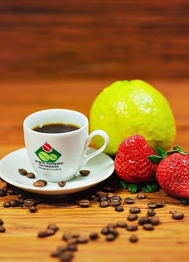 Uma xícara de café com grãos espalhados, uma fruta verde e morangos em uma superfície de madeira