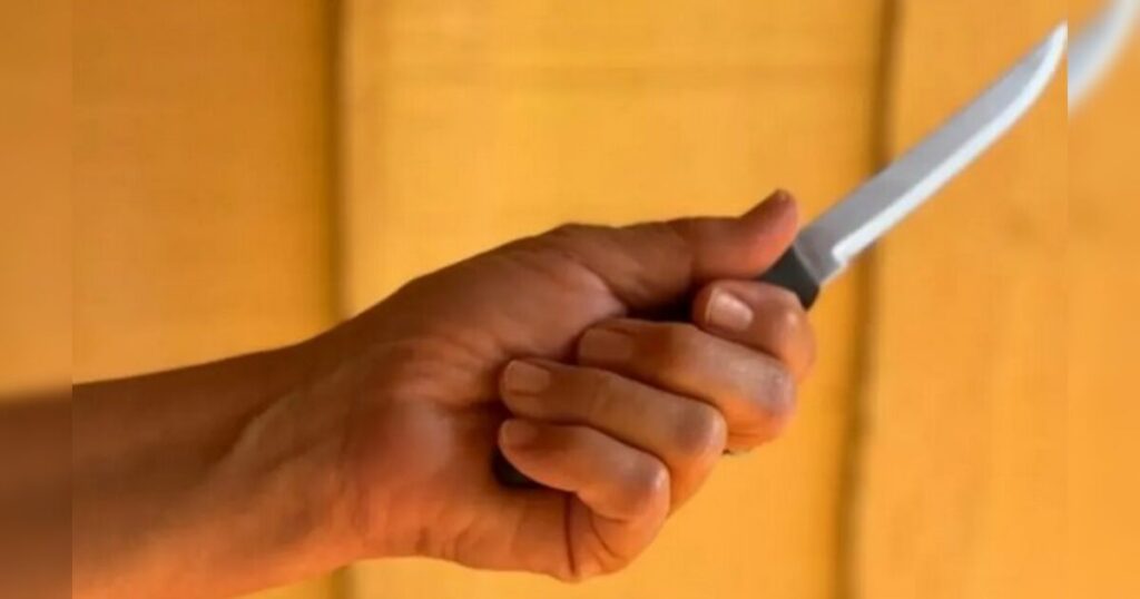 Uma mão segura uma faca com lâmina afiada contra fundo amarelo