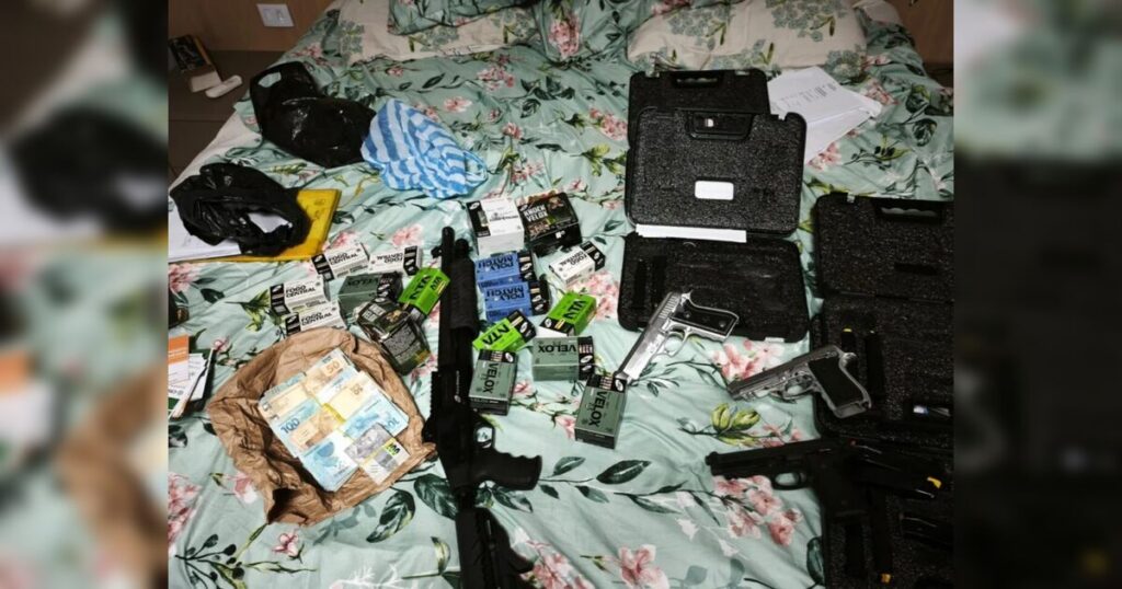 Um grupo de armas, munições e dinheiro em notas dispostos sobre uma cama com lençol estampado