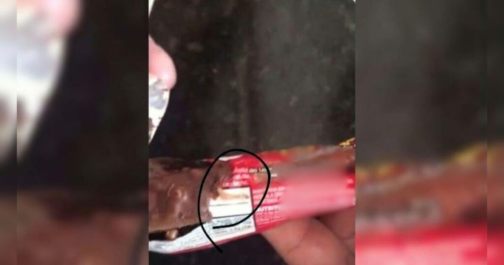 Barra de chocolate aberta com larvas visíveis dentro do produto, destacadas por círculo preto