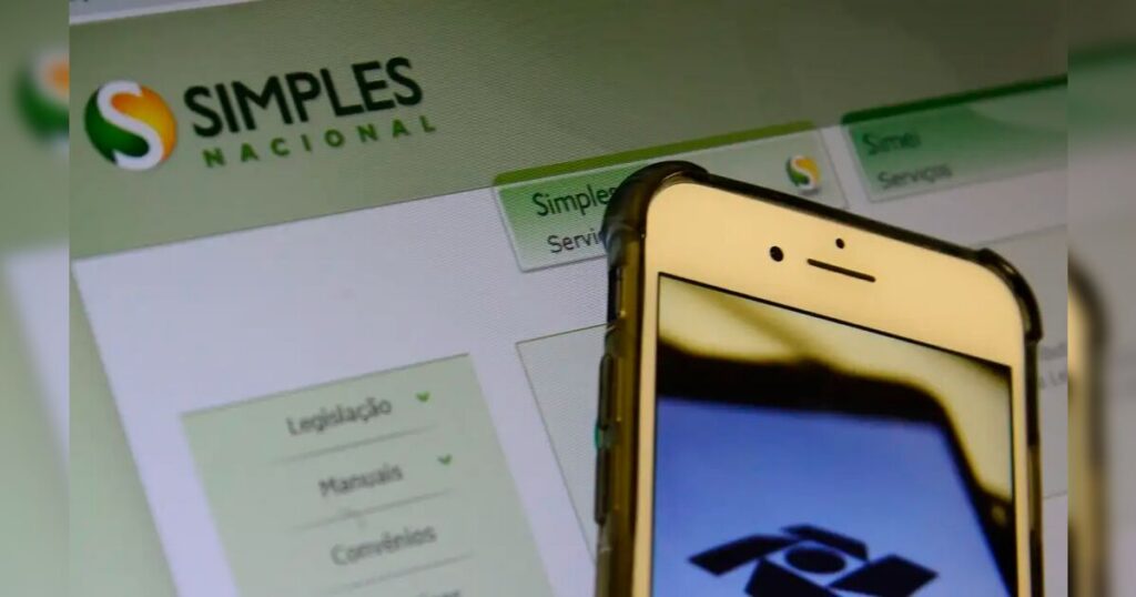 Um celular exibe o logo do Simples Nacional em frente a tela com o site do programa