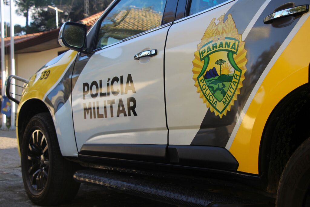 Um veículo da Polícia Militar estacionado em frente a um prédio com telhado de telhas