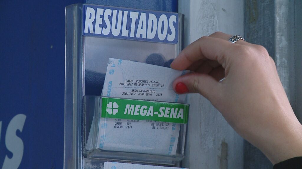 Uma mão puxa um cupom da Mega-Sena de uma caixa de resultados em local público