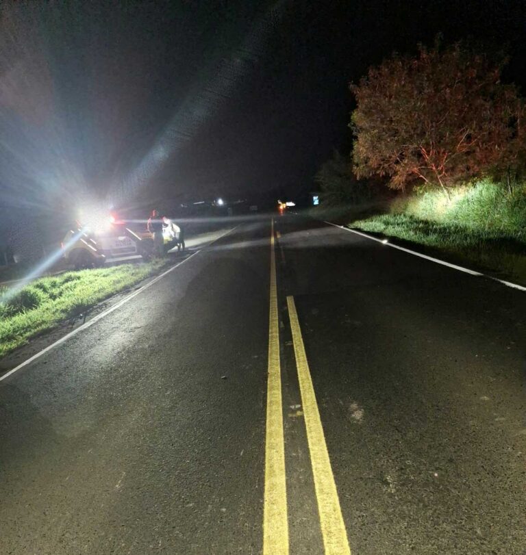 Um veículo e uma moto parados na beira de uma estrada à noite com luzes acesas