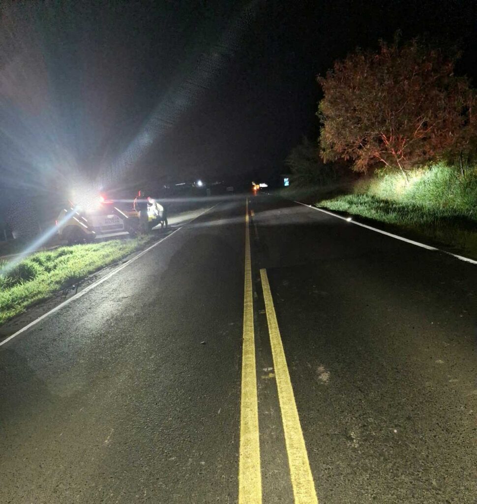 Um veículo e uma moto parados na beira de uma estrada à noite com luzes acesas