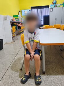 Criança sentada em cadeira de sala de aula, com o rosto desfocado