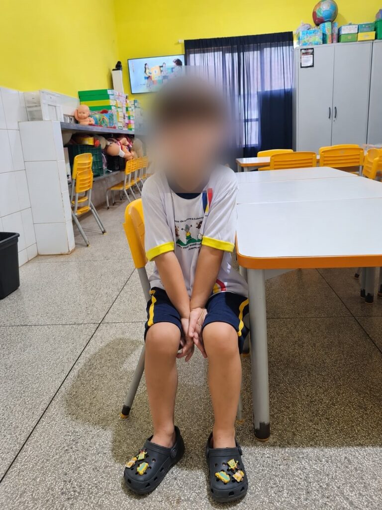 Criança sentada em cadeira de sala de aula, com o rosto desfocado