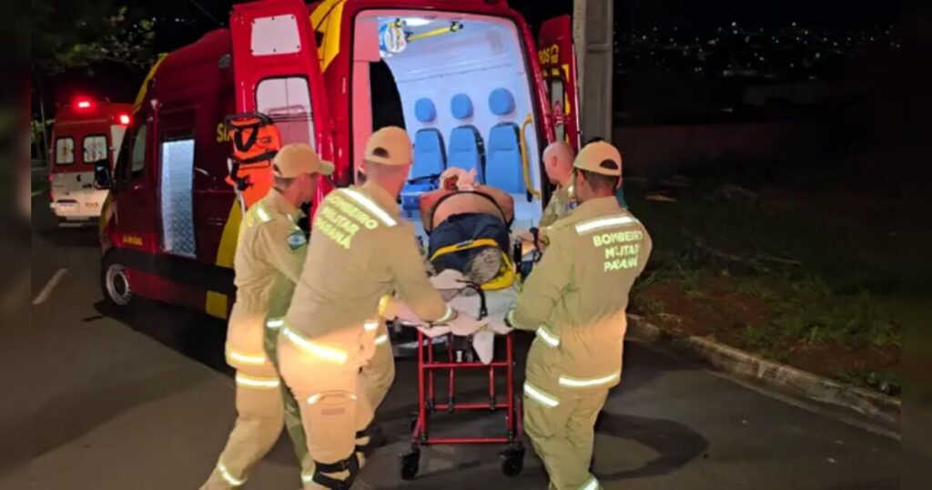 Um grupo de pessoas transporta uma pessoa em maca para uma ambulância à noite