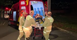 Um grupo de pessoas transporta uma pessoa em maca para uma ambulância à noite