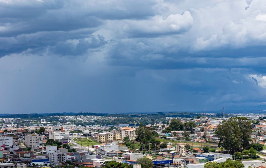 Céu nublado sobre uma cidade com edifícios e vegetação ao fundo