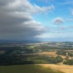 Vista aérea de campos cultivados e áreas florestadas sob céu parcialmente nublado