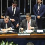 Um homem assina documento em mesa com outros homens em fundo formal