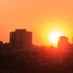 Pôr do sol sobre silhuetas de prédios em meio a céu alaranjado e intenso calor
