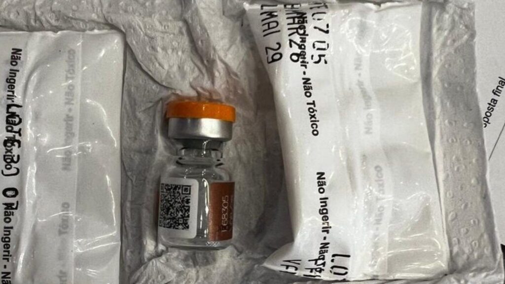 Um frasco de vidro com tampa laranja e rótulo ao lado de embalagens plásticas com texto impresso