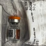 Um frasco de vidro com tampa laranja e rótulo ao lado de embalagens plásticas com texto impresso