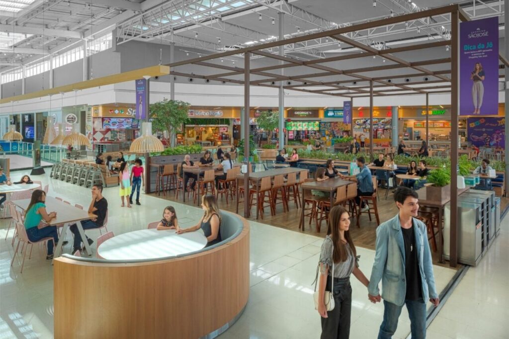 Um grupo de pessoas em um centro comercial com mesas e restaurantes ao fundo