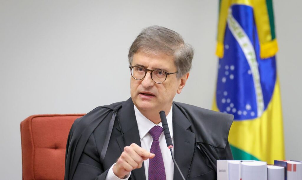 Um homem de terno e gravata fala em frente a uma bandeira brasileira em um ambiente formal