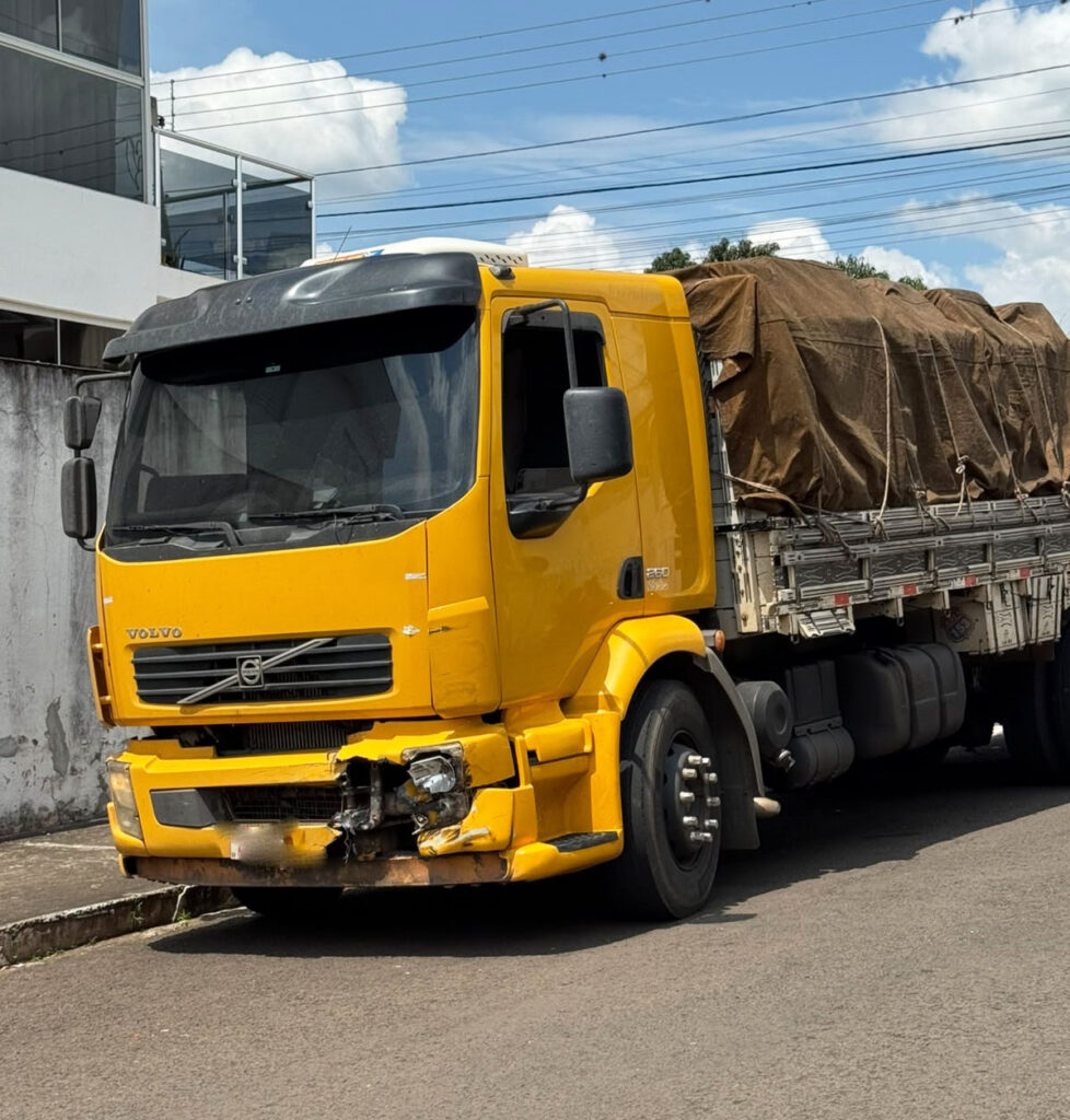 Caminhão amarelo com danos na frente parado na rua após colisão