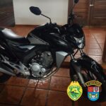 Moto preta com adesivo de aranha no para-lama dianteiro em ambiente interno com piso de cerâmica