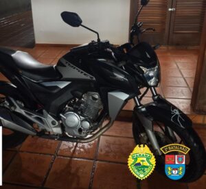 Moto preta com adesivo de aranha no para-lama dianteiro em ambiente interno com piso de cerâmica