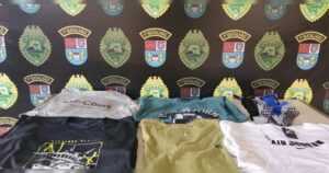 Um grupo de roupas e calçados dispostos sobre uma mesa em frente a um fundo com emblemas de instituição policial