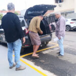 Três homens em frente a um veículo da Polícia com o porta-malas aberto em estacionamento