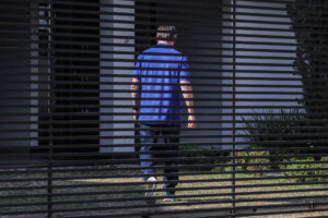 Um homem de camisa azul caminha em frente a uma grade metálica em frente a um prédio