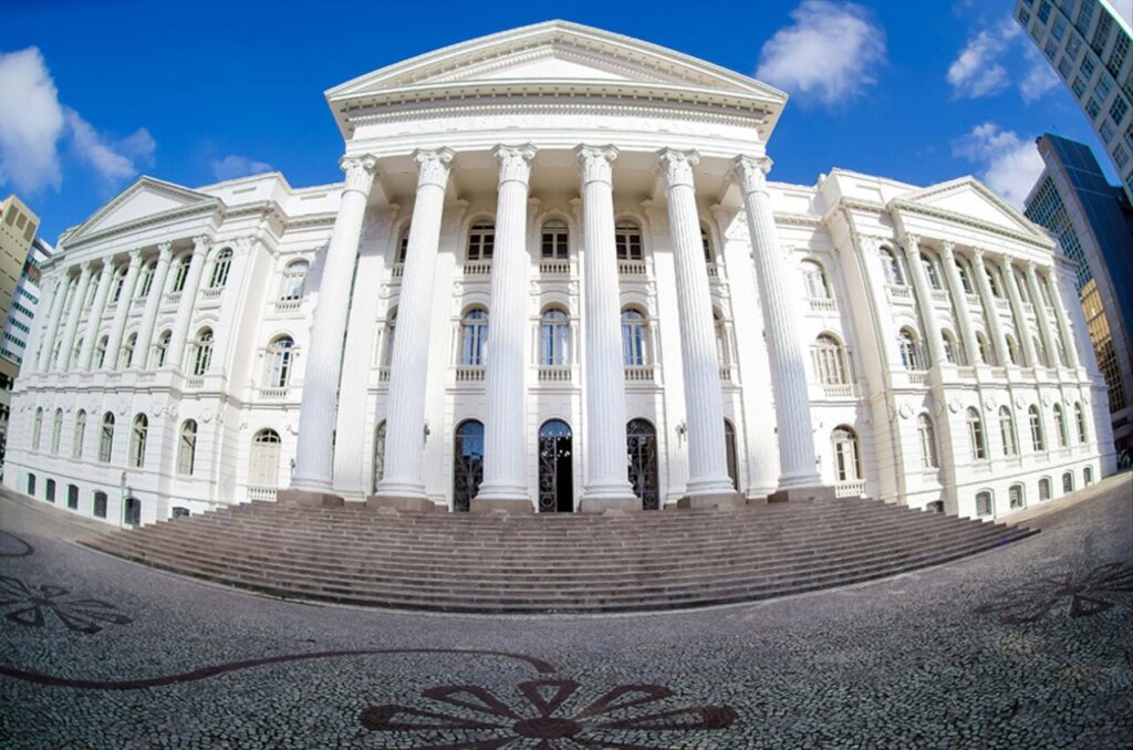 Um edifício branco com colunas e escadaria sob céu azul claro