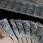 Notas de cem e duzentos reais dispostas em fãs sobre fundo escuro