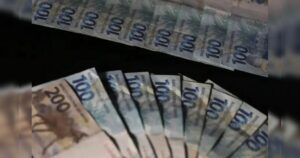 Notas de cem e duzentos reais dispostas em fãs sobre fundo escuro