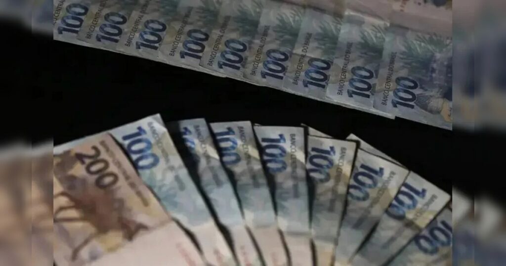 Notas de cem e duzentos reais dispostas em fãs sobre fundo escuro