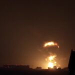 Explosão ilumina o céu noturno sobre um conjunto de edifícios em área urbana